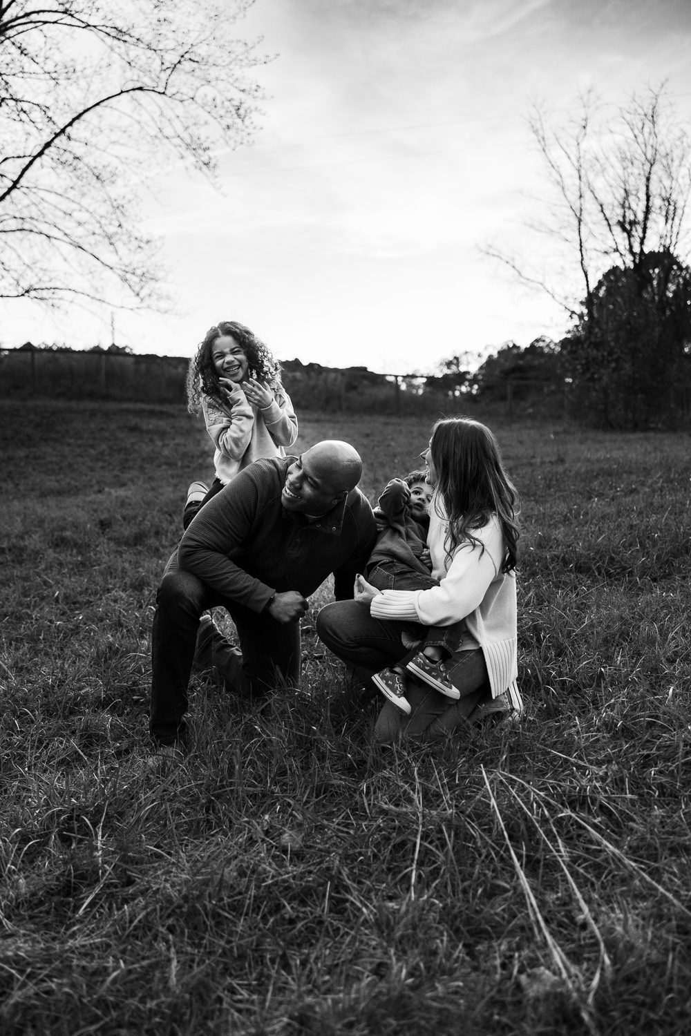 family of four laughing and climbing on each other in Birmingham Park