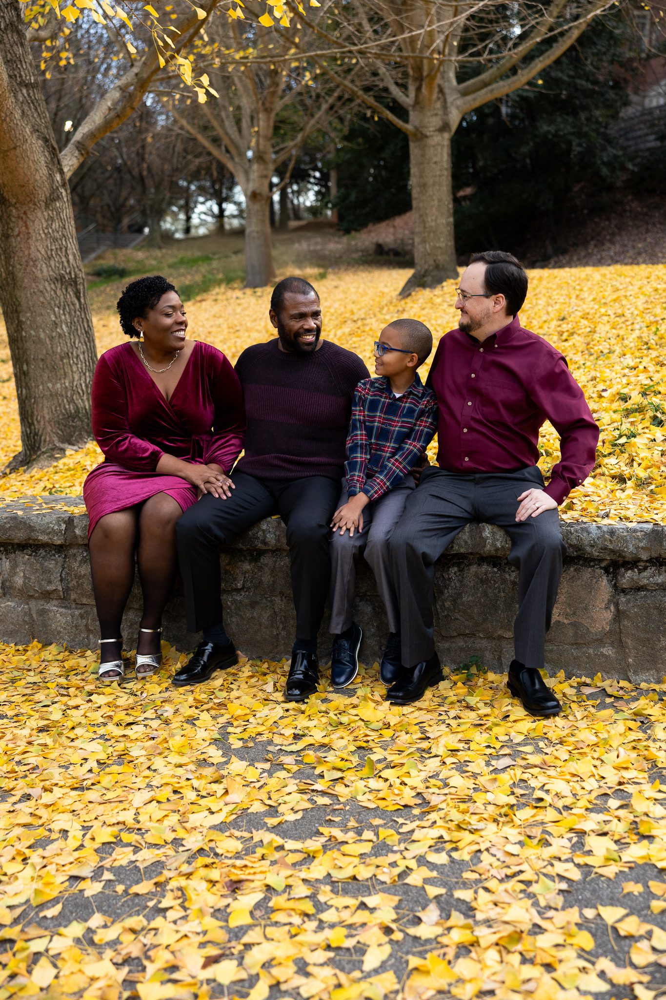 Fay family sitting together in fall leaves during Piedmont Park family photography session in Atlanta